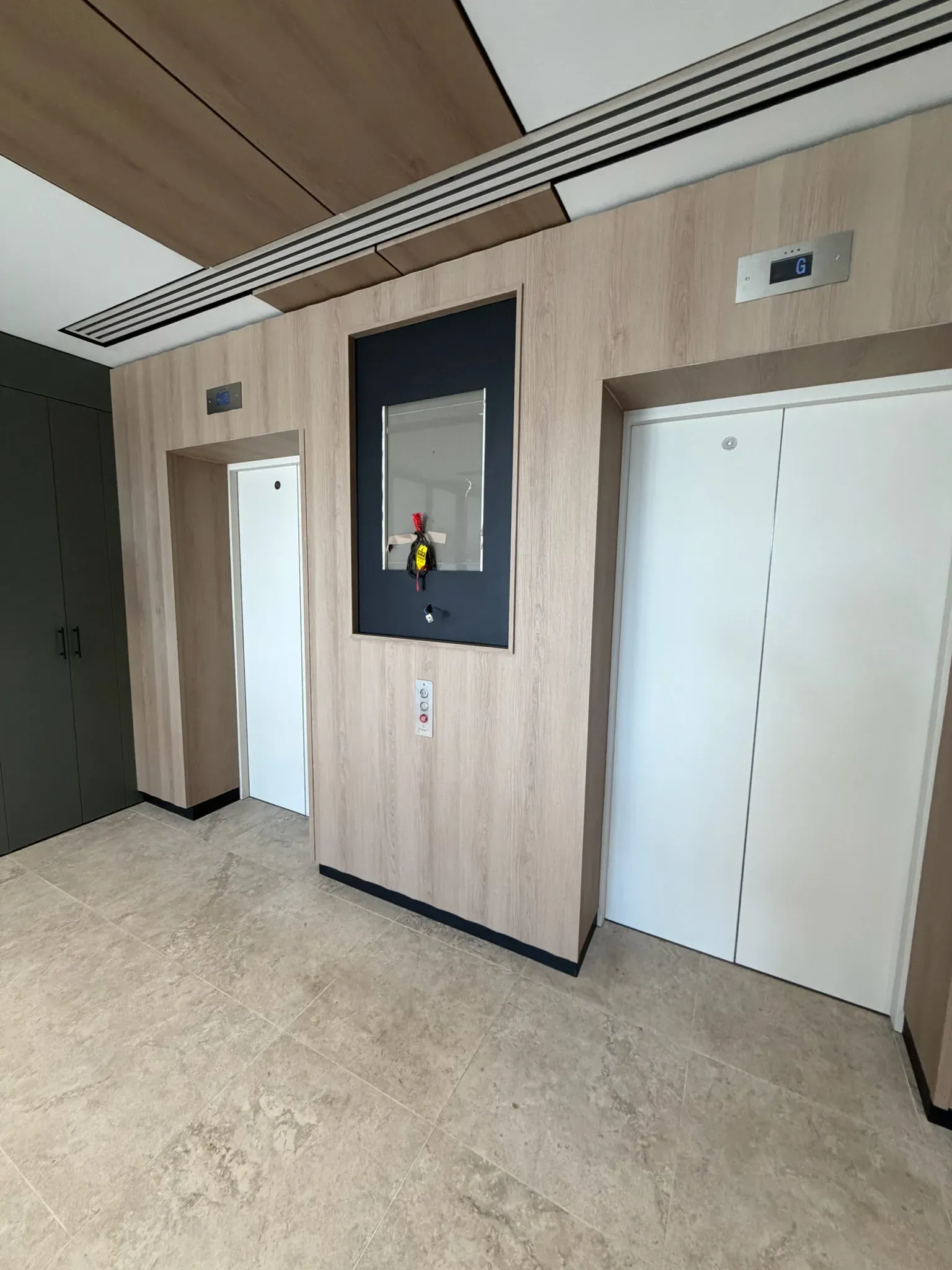 Head-on view of finished lift lobby, two wrapped lifts framing a central directory niche